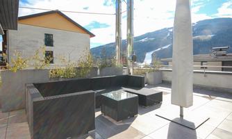 A modern terrace with a comfortable seating area and a glass table. In the background, mountains and a clear sky can be seen.