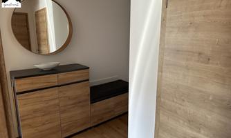 A modern foyer with a wooden piece of furniture and a round mirror. The walls are light, and the floor is made of wood.