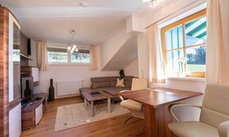 A modern living room with a comfortable sofa and a table. Large windows let in plenty of daylight and offer a view outside.