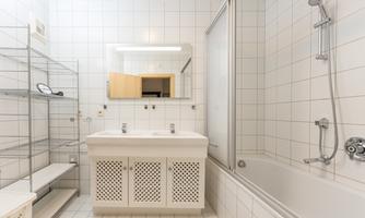 A modern bathroom with white tiles and a double sink. A bathtub and a shower are also available.