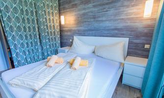 A modern bedroom with a large bed and two pillows. The walls are paneled with wood and there are decorative curtains and soft lighting.