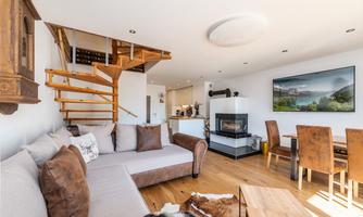 A modern living room with a cozy couch and a fireplace. In the background, there is a staircase and a dining area with wooden furniture.