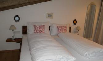A cozy bedroom with a double bed and white bed covers. Decorative mirrors and bedside lamps hang on the walls.