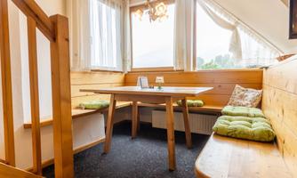 A cozy dining area with wood paneling and a table. Large windows provide plenty of daylight and a beautiful view.