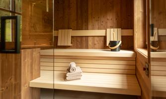 A cozy sauna room made of wood with benches and a towel. The room contains a bucket and a glass door.