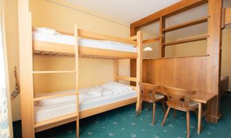 A simple room with a bunk bed and two chairs. The room has a bright color scheme and carpeted flooring.