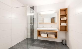 A modern bathroom with a glass shower and a large mirror. Wooden shelves provide space for fresh towels.