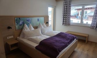 A cozy bedroom with a modern bed and decorative pillows. Large windows provide plenty of daylight.