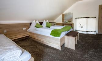 A cozy bedroom with two beds and modern wooden interiors. The pillows are green, and there is a mirror as well as plenty of daylight.