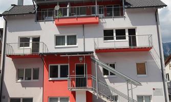 A modern residential building with gray and red facades. It has balconies and an outdoor staircase for access.