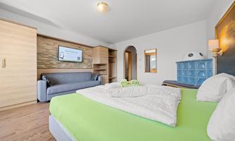 A modern bedroom with a green bed and wooden floor. There is a sofa, a television, and a stylish dresser.