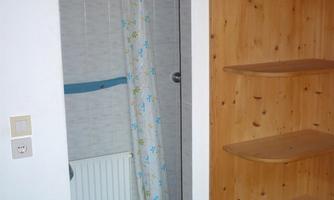 A small shower area with a bright shower curtain and a radiator. On the right, there is a wooden shelving unit with several shelves.