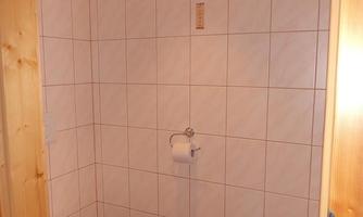 A simple bathroom with white tiles and a toilet. There is toilet paper and a blue towel on the floor.