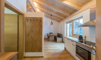 A modern, bright kitchen with wooden surfaces and exposed beams. In the background, there is a dining area with a table and chairs.
