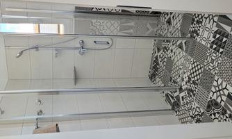 A modern shower with glass partition and an elegant, patterned floor. The walls are bright and there is a wall-mounted showerhead.