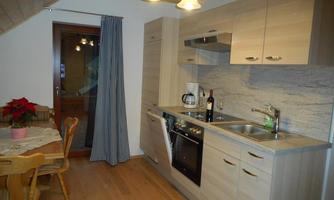 A modern kitchen with wooden shelves and an elegant table. Next to the kitchen sink, there is a bottle of wine on the countertop.