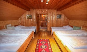 A cozy sleeping area with wooden walls and a colorful carpet. There are four beds and access to another room.