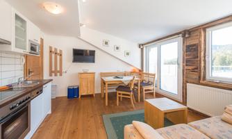 A modern apartment with an open kitchen and a cozy living area. Large windows let in plenty of daylight and offer a view outside.