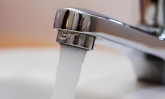 A faucet with bubbling water. The background is blurred and bright.
