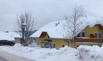 A snowy winter landscape with a yellow house and snow-covered roofs. The streets and trees are also covered with snow.