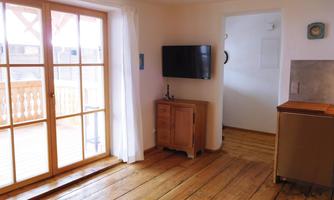A bright room with wooden floors and large windows. There is a television and a wooden table in the room.