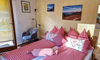 A cozy bedroom with two single beds and red and white checkered bedspreads. Pictures hang on the wall, and a new window lets in sunlight.