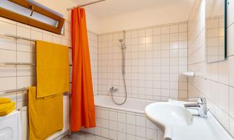 A modern bathroom with a bathtub and a shower wall. Towels are hanging on the wall and the space looks bright and clean.