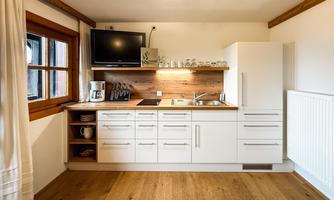 A modern kitchen with white furniture and wooden shelves. It is designed to be bright and functional, with a refrigerator and a stove.
