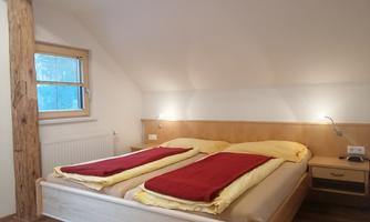 A cozy bedroom with two single beds and yellow bedcovers. The walls are light, and there is a window that lets in daylight.