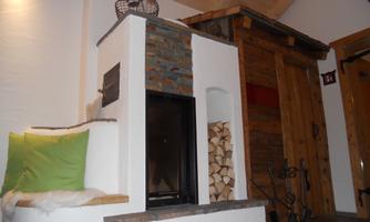 A cozy fireplace with stone elements and stacked firewood. In the background, wooden paneling is visible, creating a warm atmosphere.