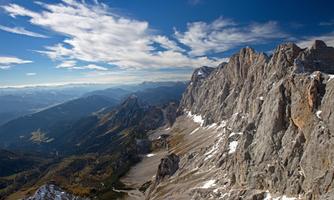 An impressive mountain landscape with rugged rocks and snow-capped peaks. The sky is blue and interspersed with a few clouds.