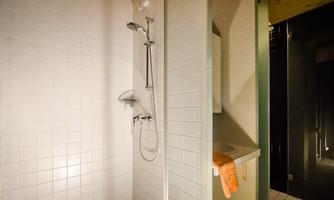 A modern bathroom with a shower and white tiles. There is a washbasin and a towel on the shelf.