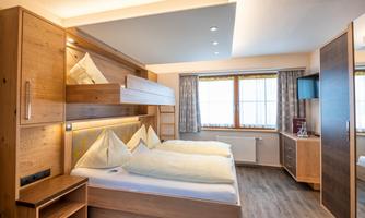 A modern room with wooden paneling and two beds. The room has large windows and a cozy atmosphere.