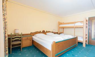 A simple room with a double bed and a bunk bed. There is a table and chairs made of wood.