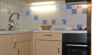 A modern kitchen with wooden cabinets and a stove. The walls are decorated with blue and white tiles.