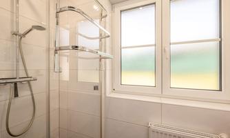 A bright shower with a glass partition and modern fixtures. The window has frosted glass panes that let soft light in.