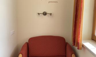 A cozy red armchair is placed in a corner of a room. On the wall above the armchair, there is a saying about laughter.