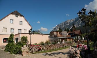 A picturesque village with traditional buildings and a view of the mountains. The street is lined with flowers and a well-maintained environment.