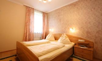 A cozy bedroom with a double bed and soft beddings. The walls are painted in gentle colors, and there is a small nightstand next to the bed.