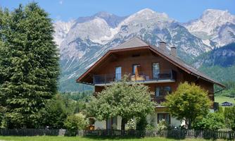 A beautiful house with a garden in front of majestic mountains. The surroundings are green and picturesque.