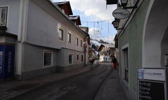 A quiet street in a picturesque village, surrounded by traditional buildings. Christmas lights hang over the street, creating a festive atmosphere.