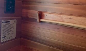 A sauna interior with wooden paneling and a display for temperature monitoring. On the wall, there is a wooden strip for relaxation.