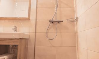 A modern bathroom with a shower, wood flooring, and a large mirror. The walls are in warm beige and brown tones.