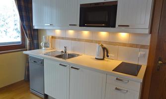 A modern kitchen with white cabinets and wooden surfaces. It is equipped with a sink, a microwave, and a dishwasher.