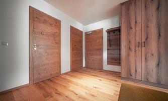 A modern foyer with wooden flooring and several wooden doors. The walls are painted light and there is a small area for coats.