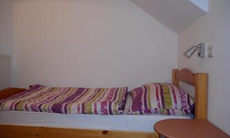 A simple bedroom with a bed and a small table. The bedspread has a striped pattern in various colors.