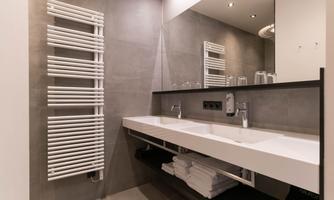 A modern bathroom with a double sink and a large mirror. The room has gray walls and a towel radiator.