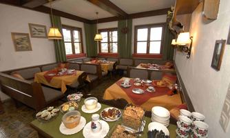 A cozy breakfast room with tables covered in orange tablecloths. On one table, there is a diverse buffet with various foods and drinks.