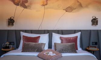 A stylish bedroom with two beds, decorated with colorful cushions. On the wall, there is a gentle floral pattern and a warm color scheme.