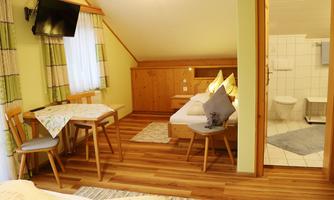 A cozy holiday apartment with wooden floors, a table and chairs, as well as a sitting area. The room has windows that let in plenty of light, and a bathroom is visible.